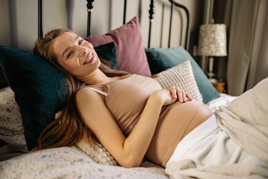 A happy pregnant couple looking at a baby name book together in a bright, cozy living room.
