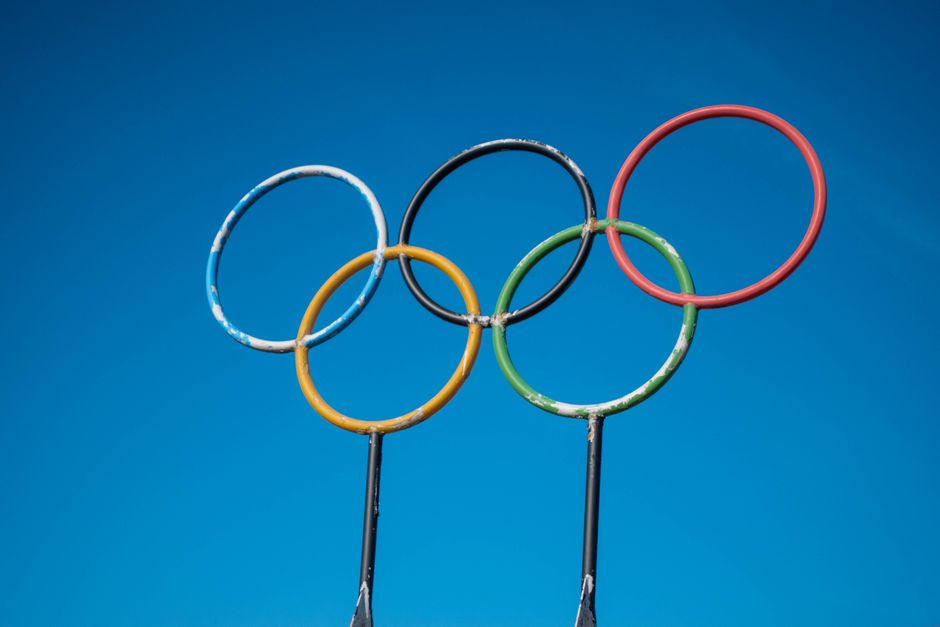 A collection of Olympic enamel pins displayed across an athlete lanyard beside a glowing smartphone screen