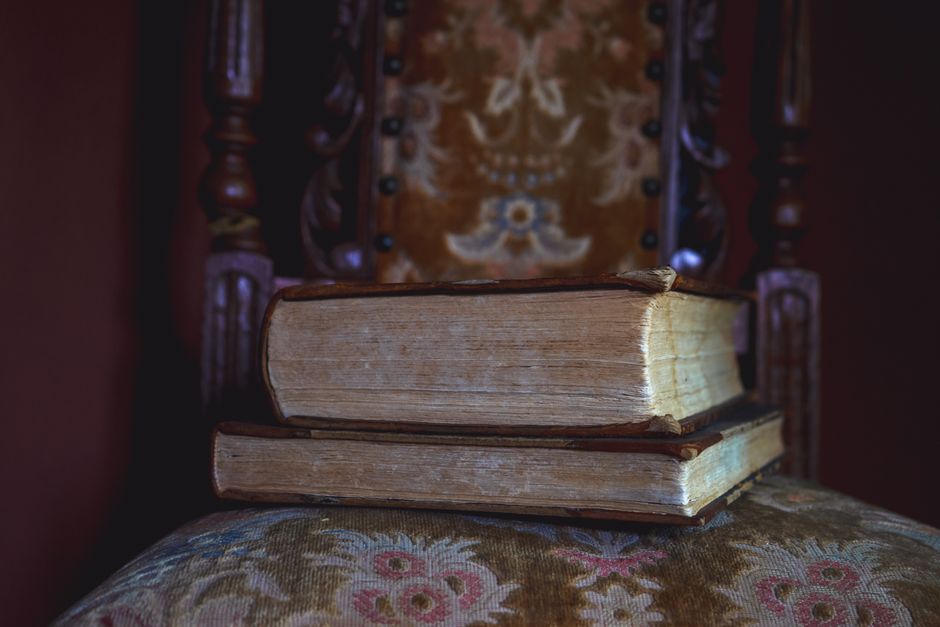 Antique leather-bound grimoire resting beside dried roses on an ornate mahogany desk