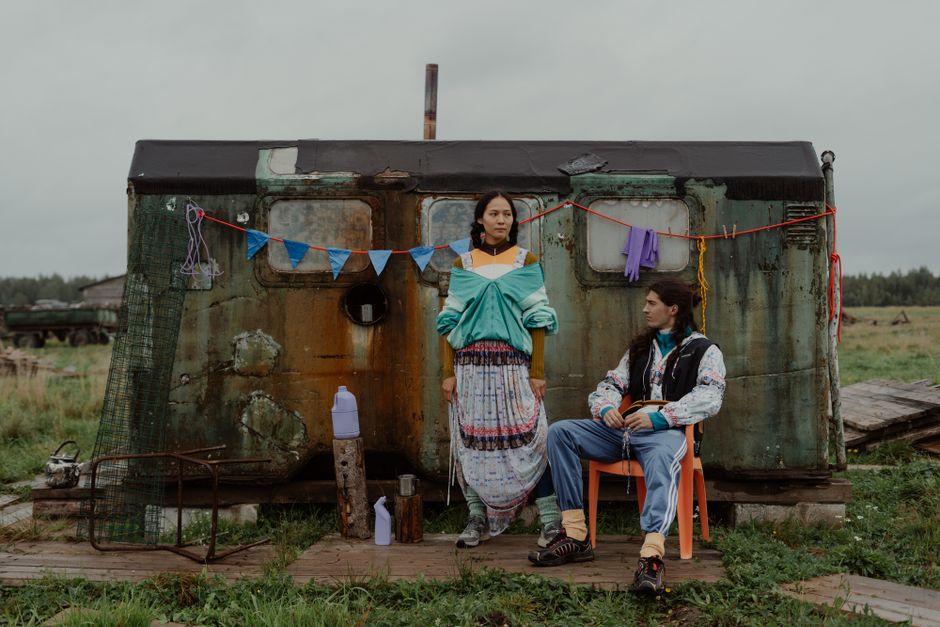 Nomadic couple sitting outside a camper van drinking coffee beneath mountain peaks