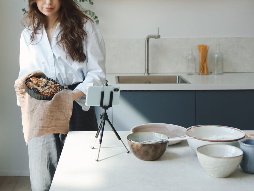 Top-down view of an aesthetic cooking desk with ingredients, utensils, and smartphone setup on a tripod